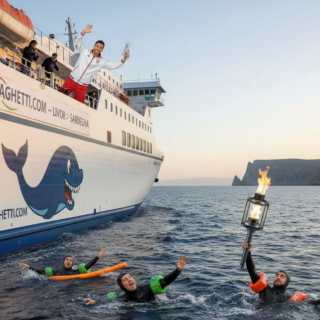 Tedofori con la Torcia Olimpica nuotano nel mare, mentre un passeggero felice li saluta dal ponte di un traghetto Moby in partenza da Livorno per la Sardegna al tramonto